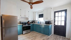 Uma cozinha moderna com armários verde-água, geladeira de aço inoxidável, fogão e ventilador de teto.