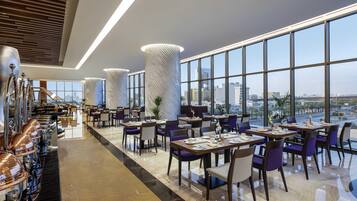 Un restaurant moderne doté d’un long comptoir, de hauts plafonds et de grandes fenêtres offrant une vue sur la ville.