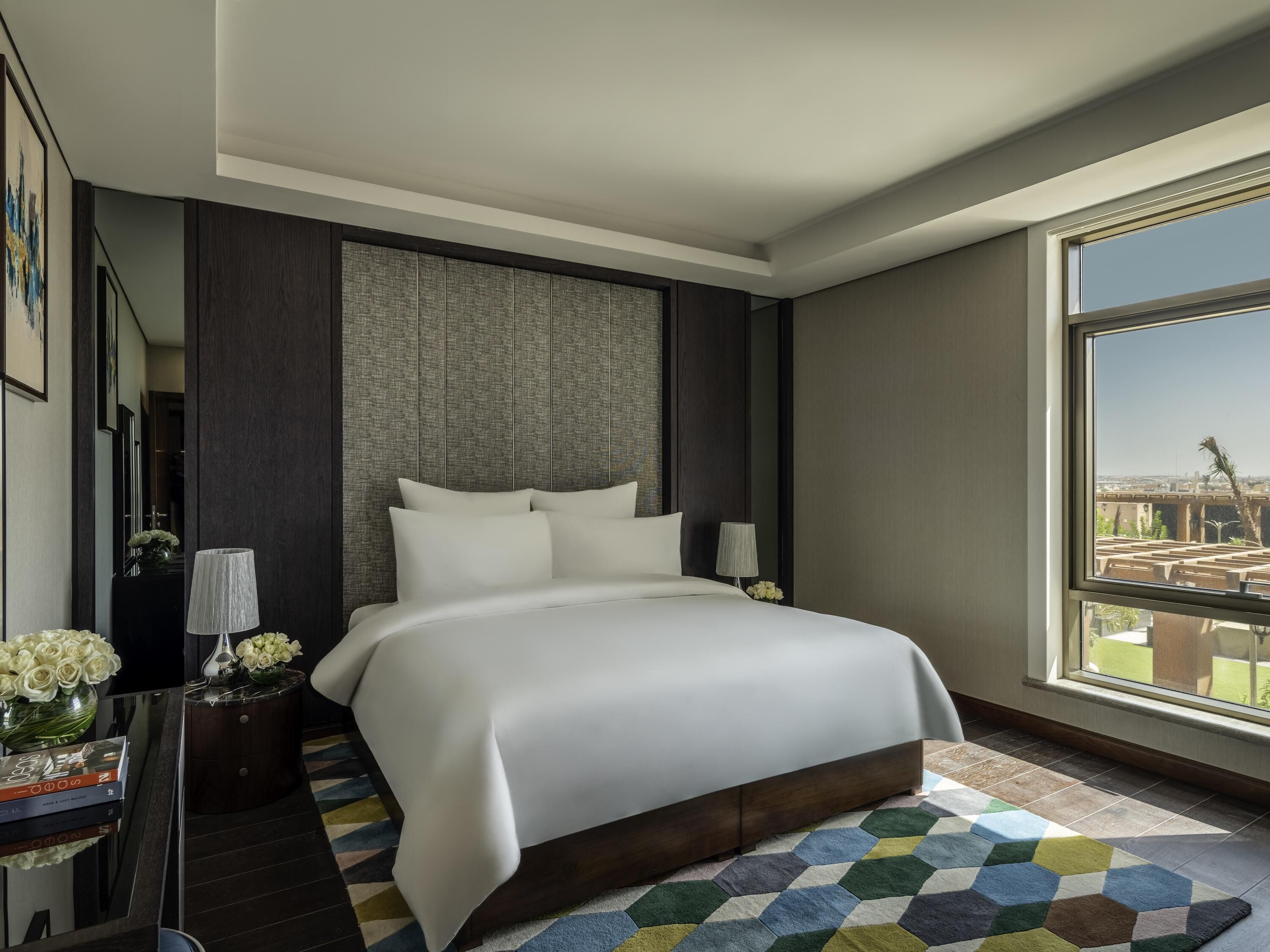 Une chambre d’hôtel moderne avec un grand lit, une vue sur la ville et un tapis aux motifs géométriques.