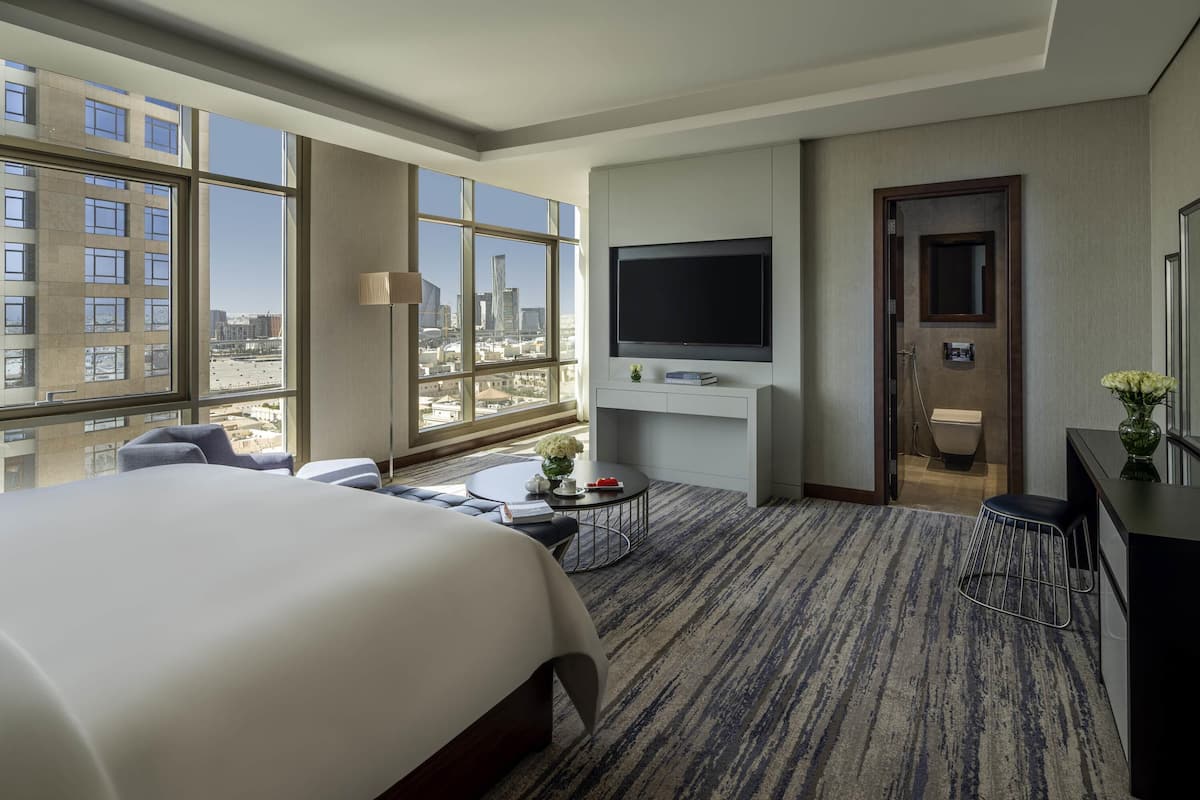 Una habitación de hotel moderna con una cama grande, un televisor de pantalla plana, un escritorio y vistas de la ciudad a través de amplias ventanas.