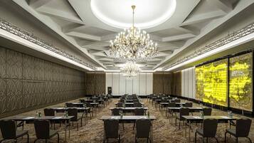 A conference room with a chandelier, tables, chairs, and a large screen.