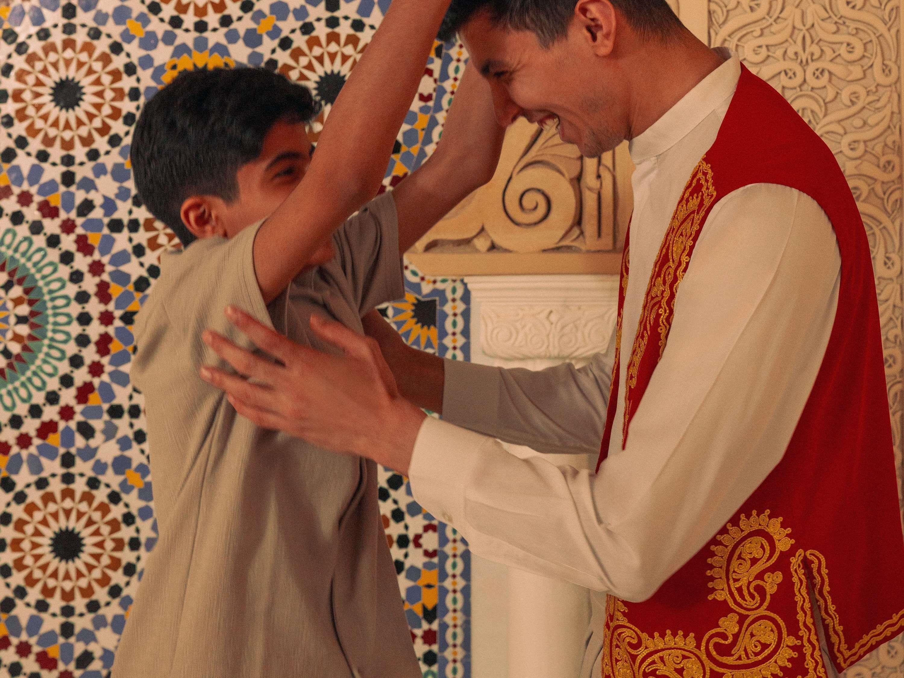 A person in a white shirt and red vest interacting with another individual in a patterned background.