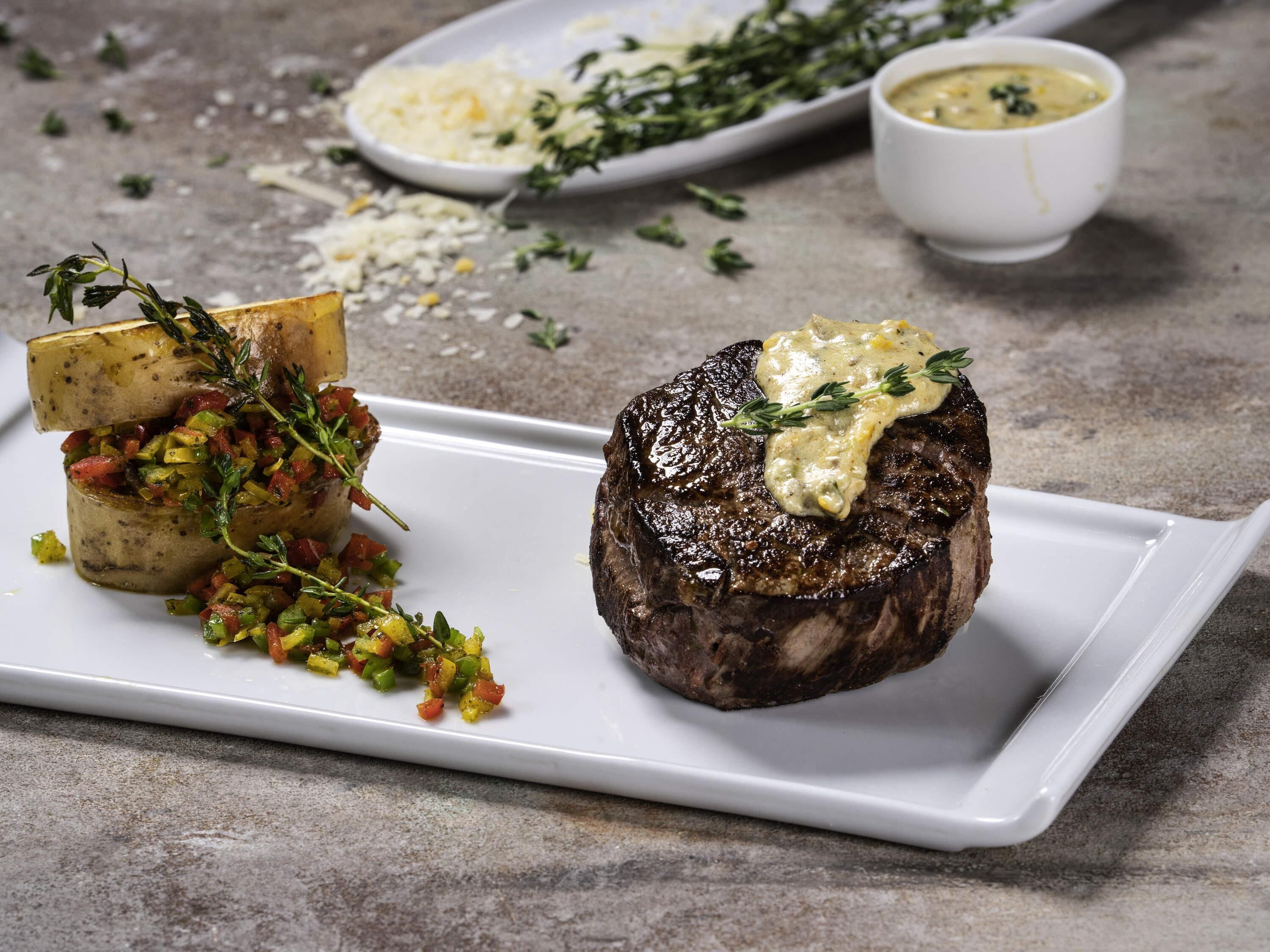 A steak with a creamy sauce and a side of diced vegetables on a white plate.
