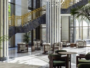 A spacious lobby with a marble floor, a staircase with golden railings, and seating areas with cushions.