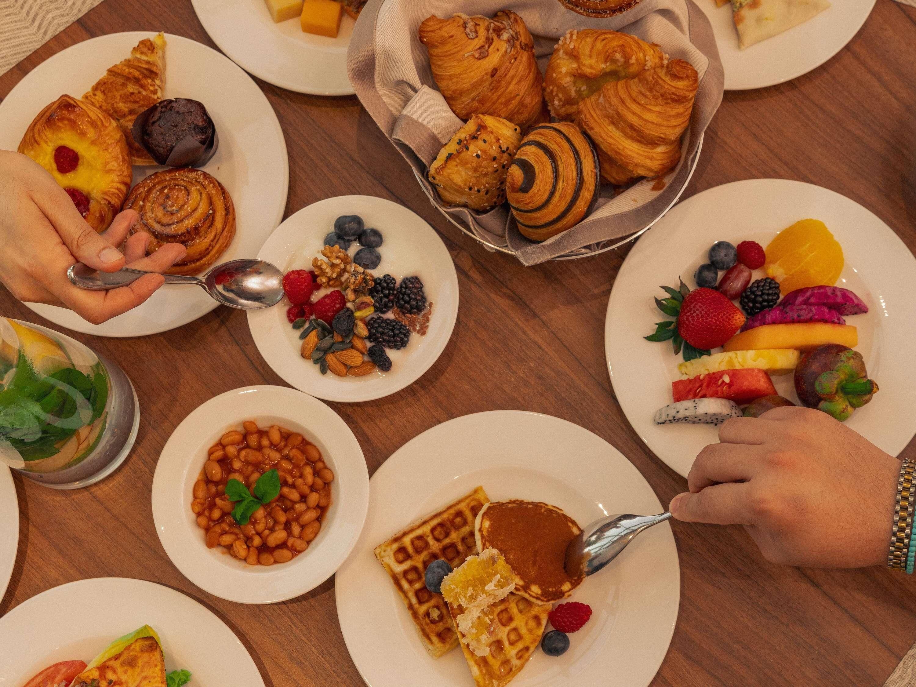 A breakfast buffet with various pastries, fruits, and waffles.