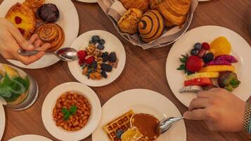 A breakfast buffet with various pastries, fruits, and waffles.