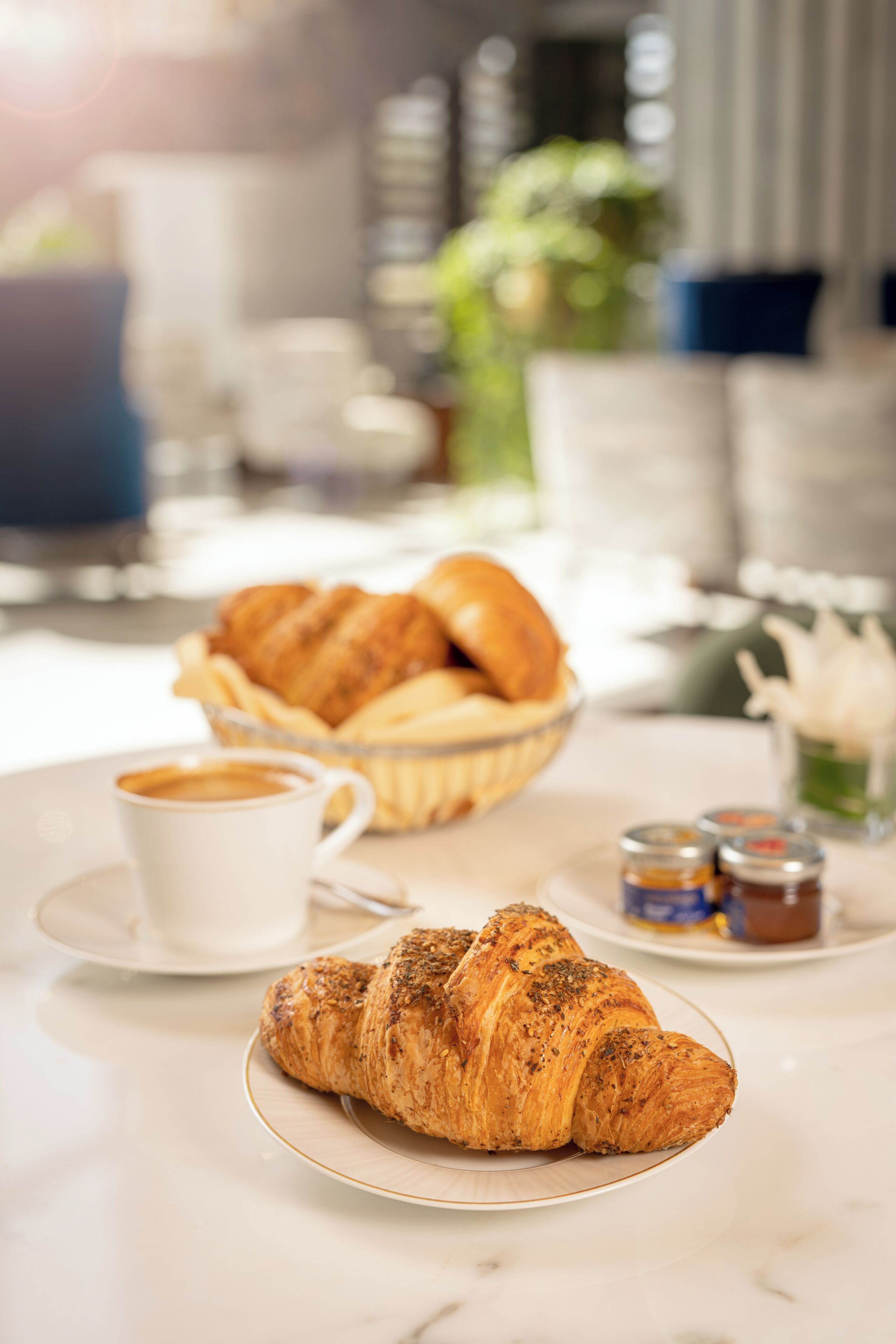 A breakfast setting with croissants, a cup of coffee, and condiments on a marble table.