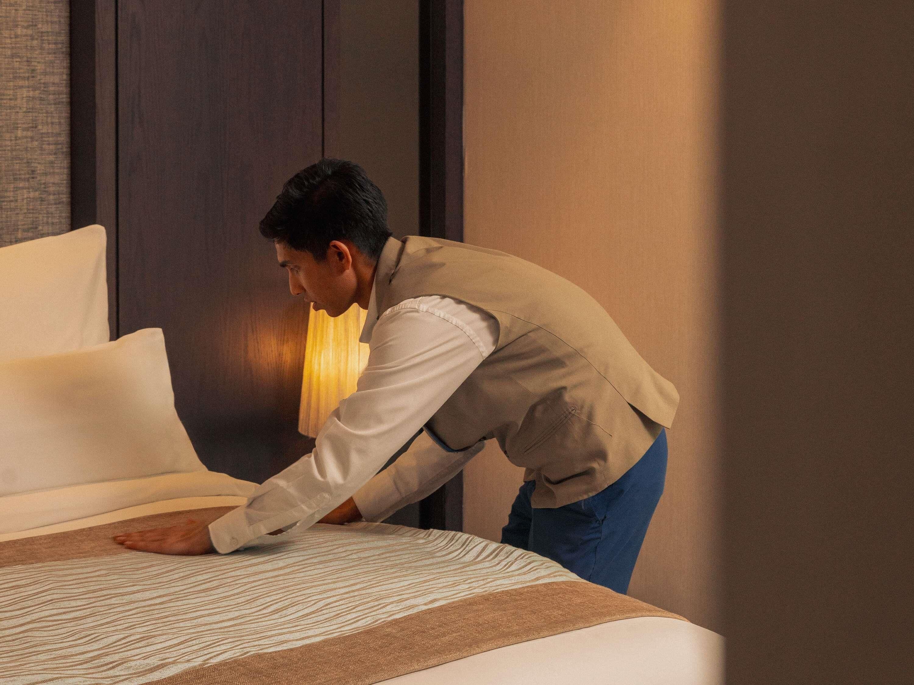 A person adjusting a bed in a room with a dark wooden headboard and a lamp.
