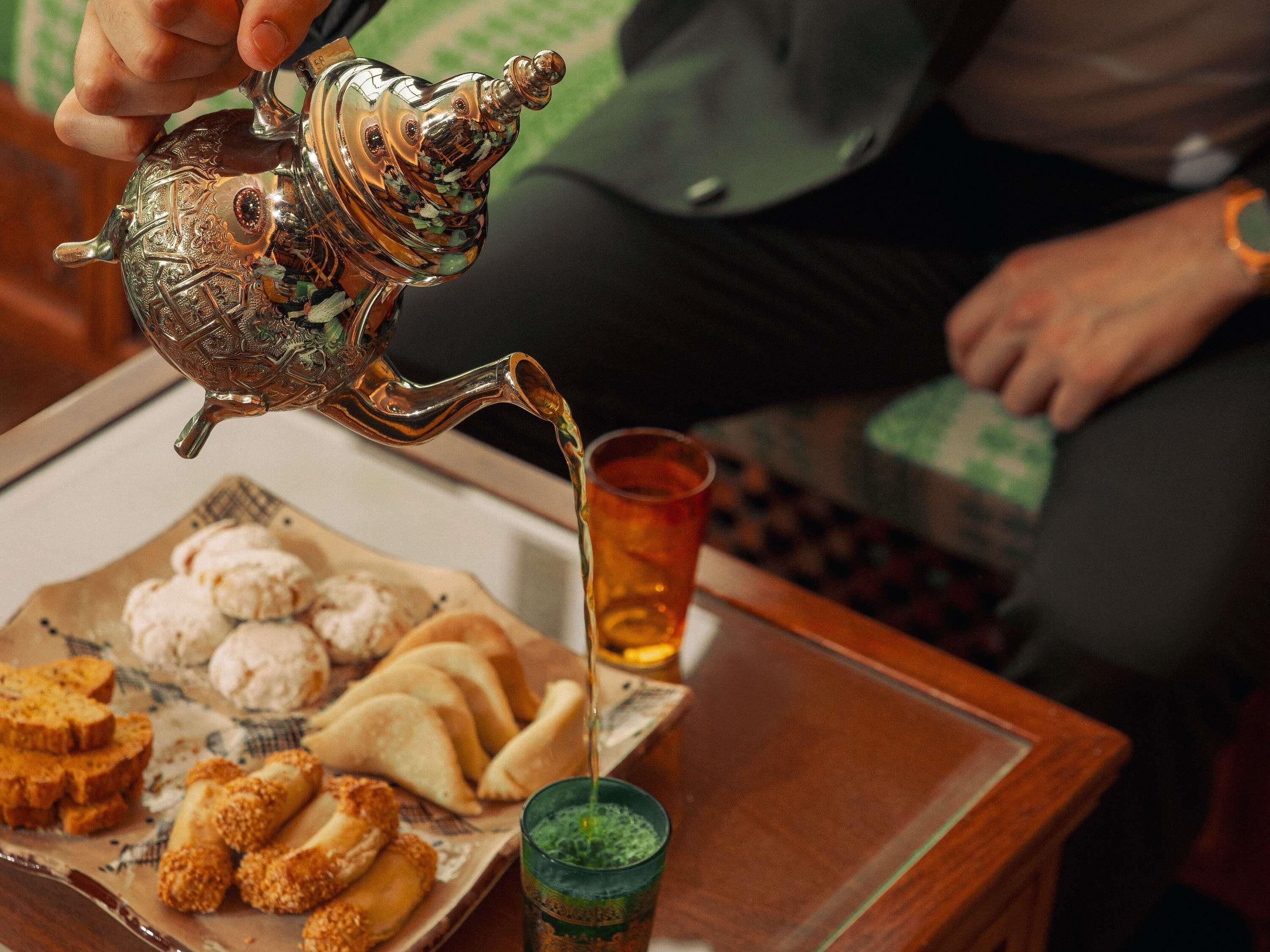 A person pouring tea from an ornate metal teapot onto a plate with food.