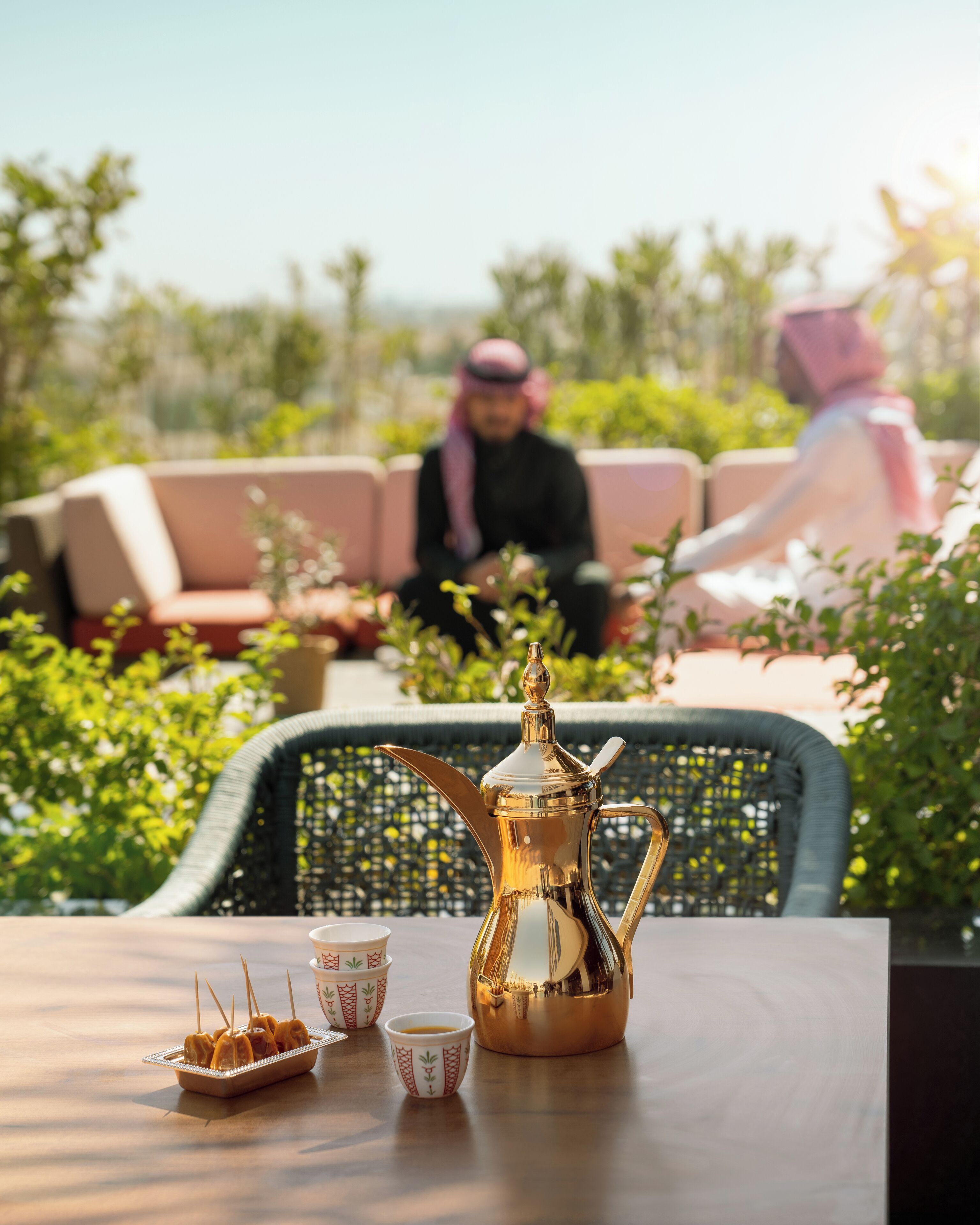 Une table avec une théière et des tasses dorées, un plateau de friandises et une chaise en osier.