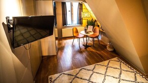 A compact room with a TV mounted on the wall, a small dining table with two chairs, a radiator, and a window with curtains. - Bambu Sleep Boutique double room 4 (Haarlem)