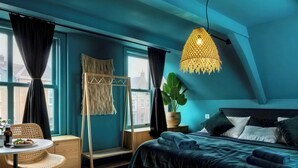 A bedroom with a bed, a hanging light fixture, a window with curtains, a plant, and a small table with a chair. - Bambu Sleep Boutique double room 3 (Haarlem)