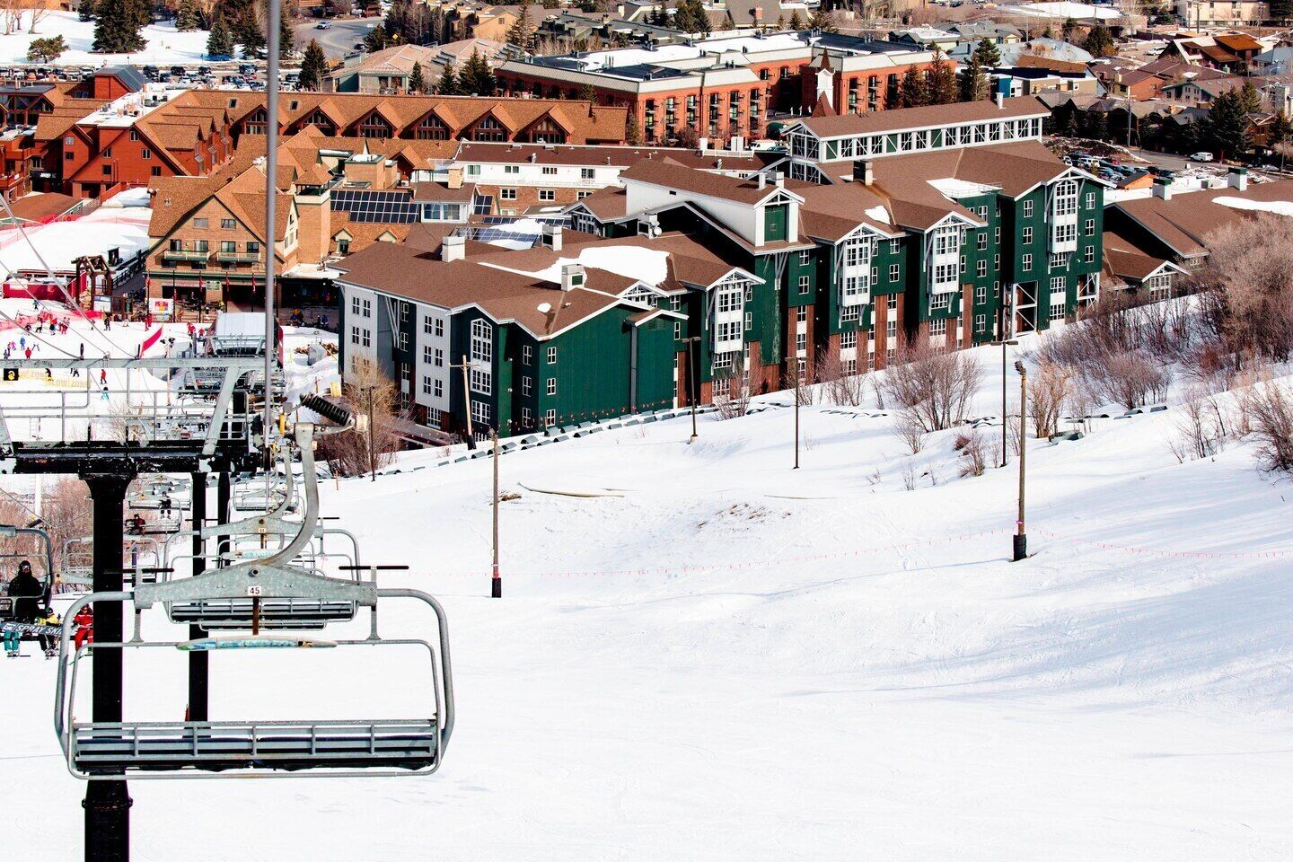 A ski lift with a chairlift and a snowy landscape with buildings in the background.