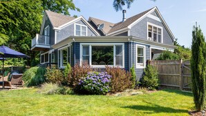 A two-story house with a covered porch, a fenced backyard, and a variety of plants and shrubs. - Enjoy Newport, stunning beaches, hot-tub, & relax at the lovely Coastal Hideaway (Middletown)