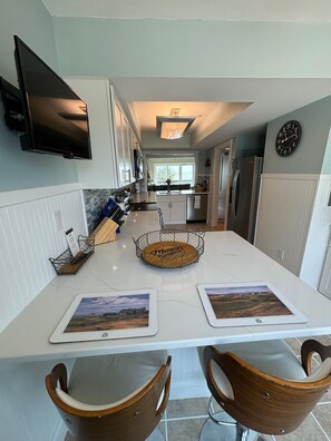 A modern kitchen with a central island, white cabinetry, a flat-screen TV mounted above the island, and a clock on the wall.