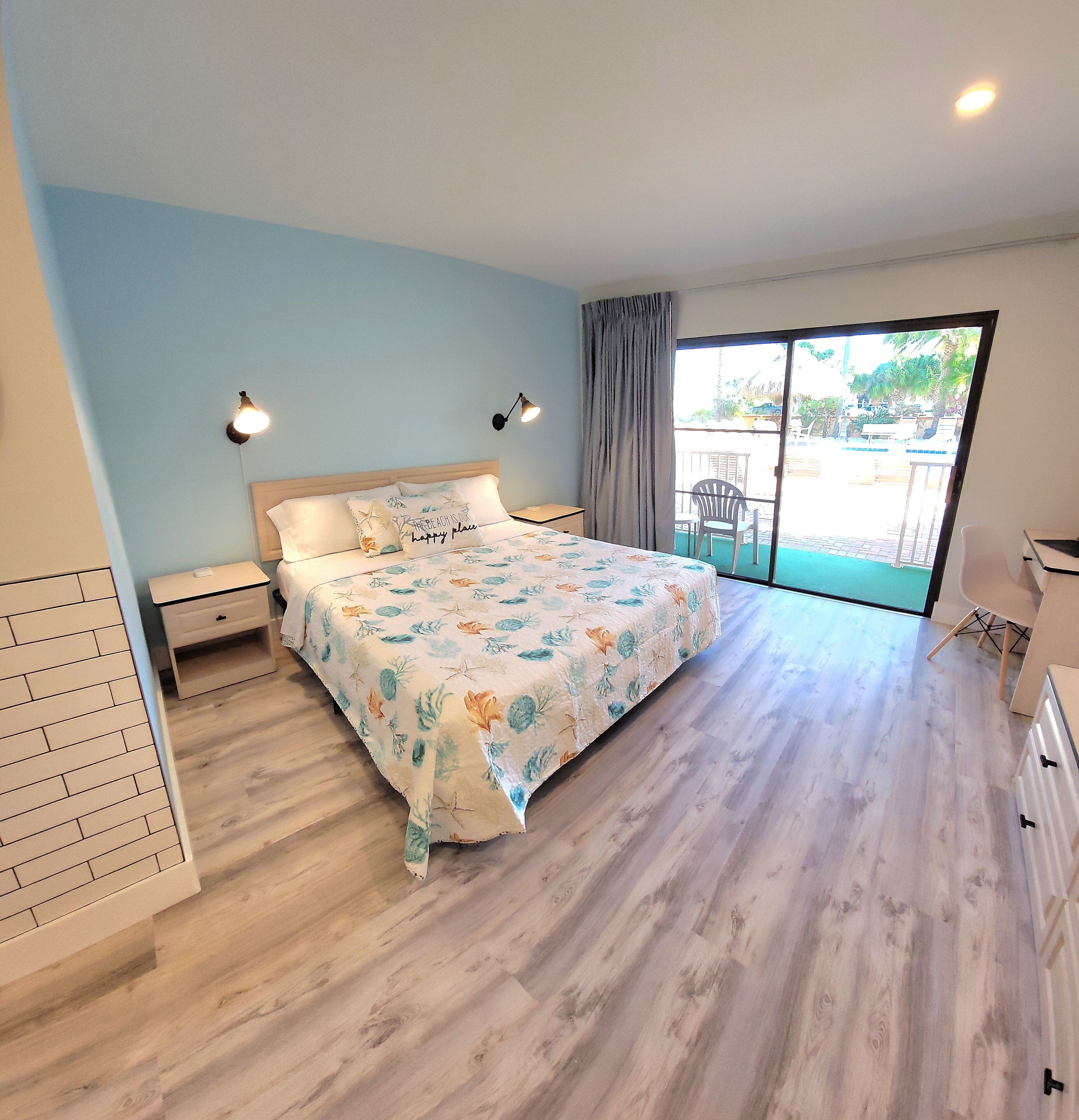 Un dormitorio con una cama, dos lámparas de noche, una mesita de noche, una ventana con vistas al exterior y una puerta corrediza de vidrio que da a un balcón.