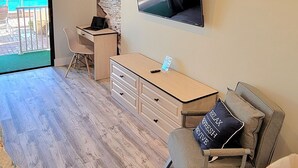 Moderni olohuone, jossa on puulattia, työpöytä, mukava nojatuoli, seinälle asennettu televisio ja näkymä ulos.