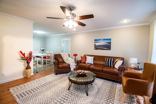 A living room with a brown leather sofa, a glass coffee table, a patterned rug, and a ceiling fan. - The "Hartwell" House (Hartwell)