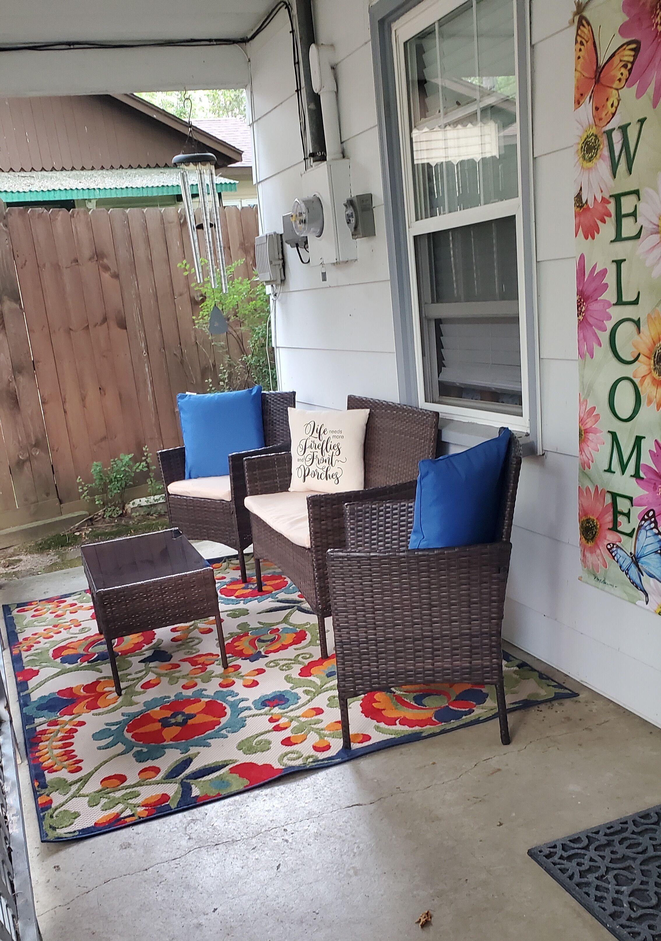 A patio with wicker furniture, a colorful rug, and a 'WELCOME' sign.