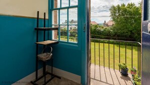 A room with a teal door and window, a small chair, and a view of a garden and houses. - Rosebery Place in the Heart of Gullane (Gullane)