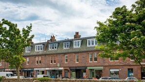 A traditional brick building with multiple shops on the ground floor, including a pharmacy and a kitchen store. - Rosebery Place in the Heart of Gullane (Gullane)