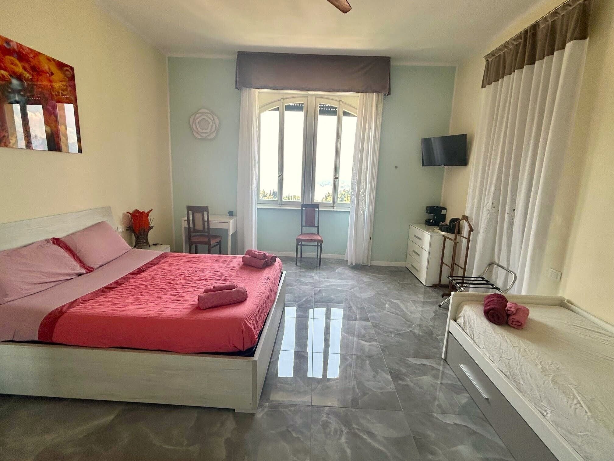 A bedroom with a bed, a desk, a chair, a TV, and a window with curtains.