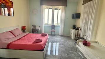 A bedroom with a bed, a desk, a chair, a TV, and a window with curtains.
