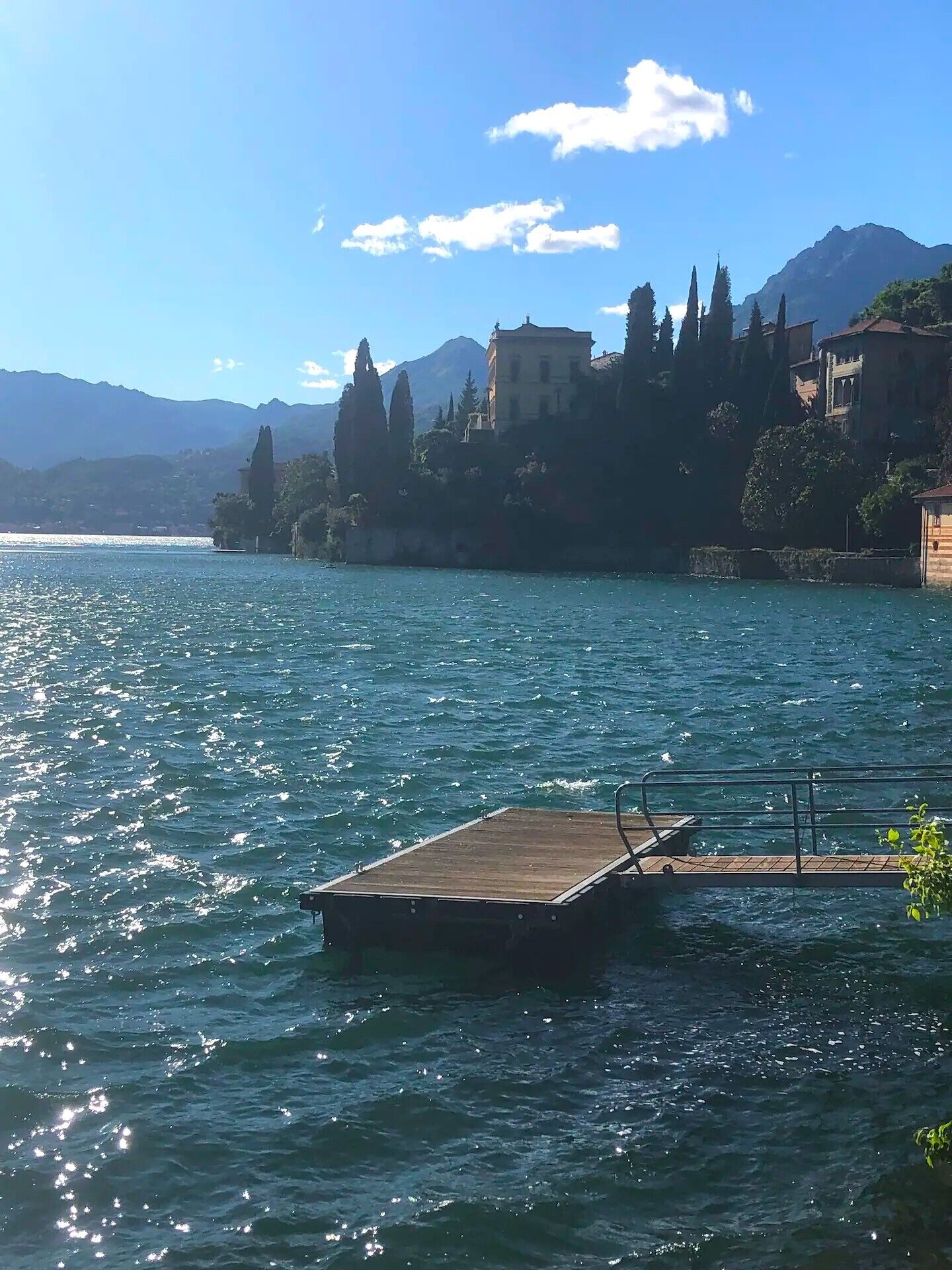 A wooden dock extending into a calm lake with a backdrop of mountains and buildings.