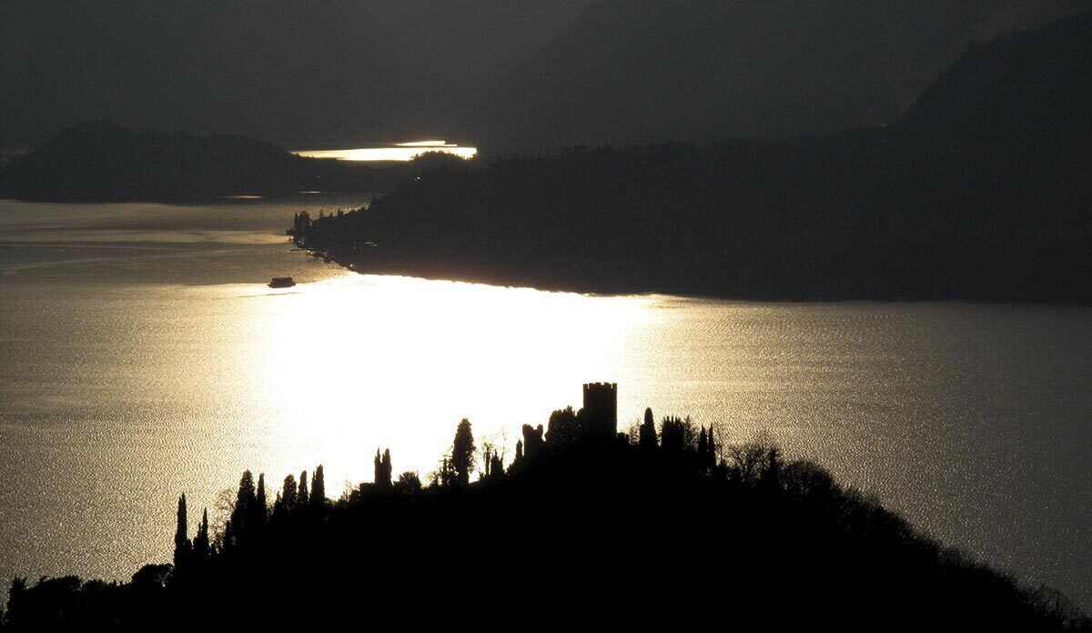 A silhouette of a castle on a hill overlooking a calm lake at sunset.