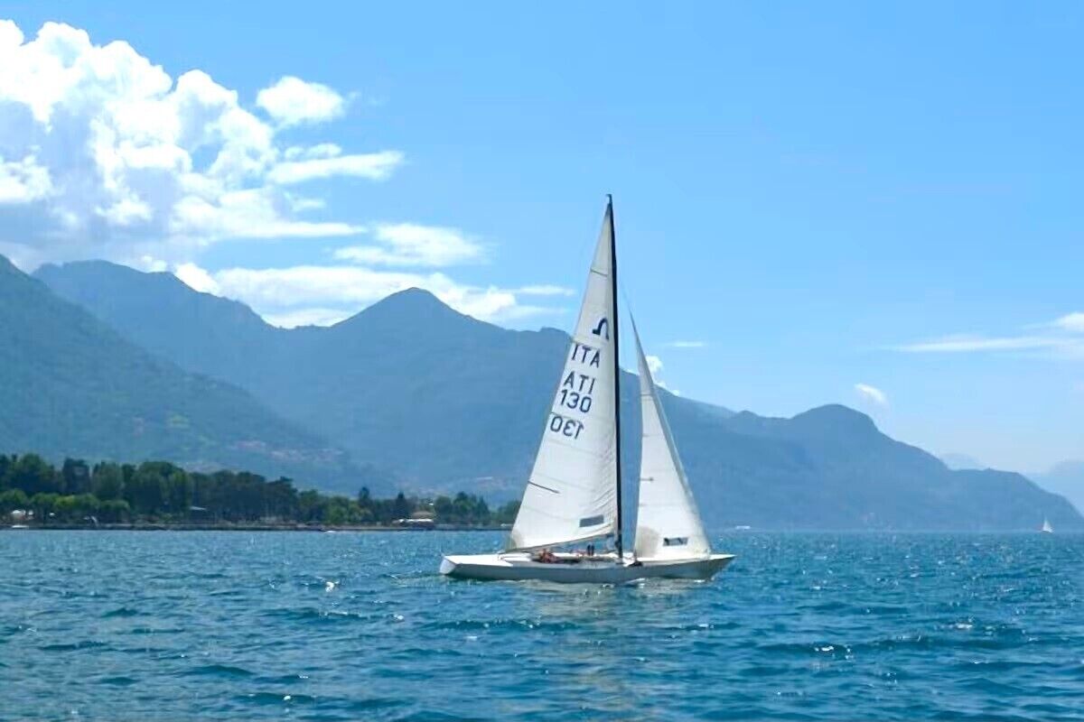 Een zeilboot met registratienummer 'ATI 130' op een wateroppervlak, met bergen op de achtergrond.