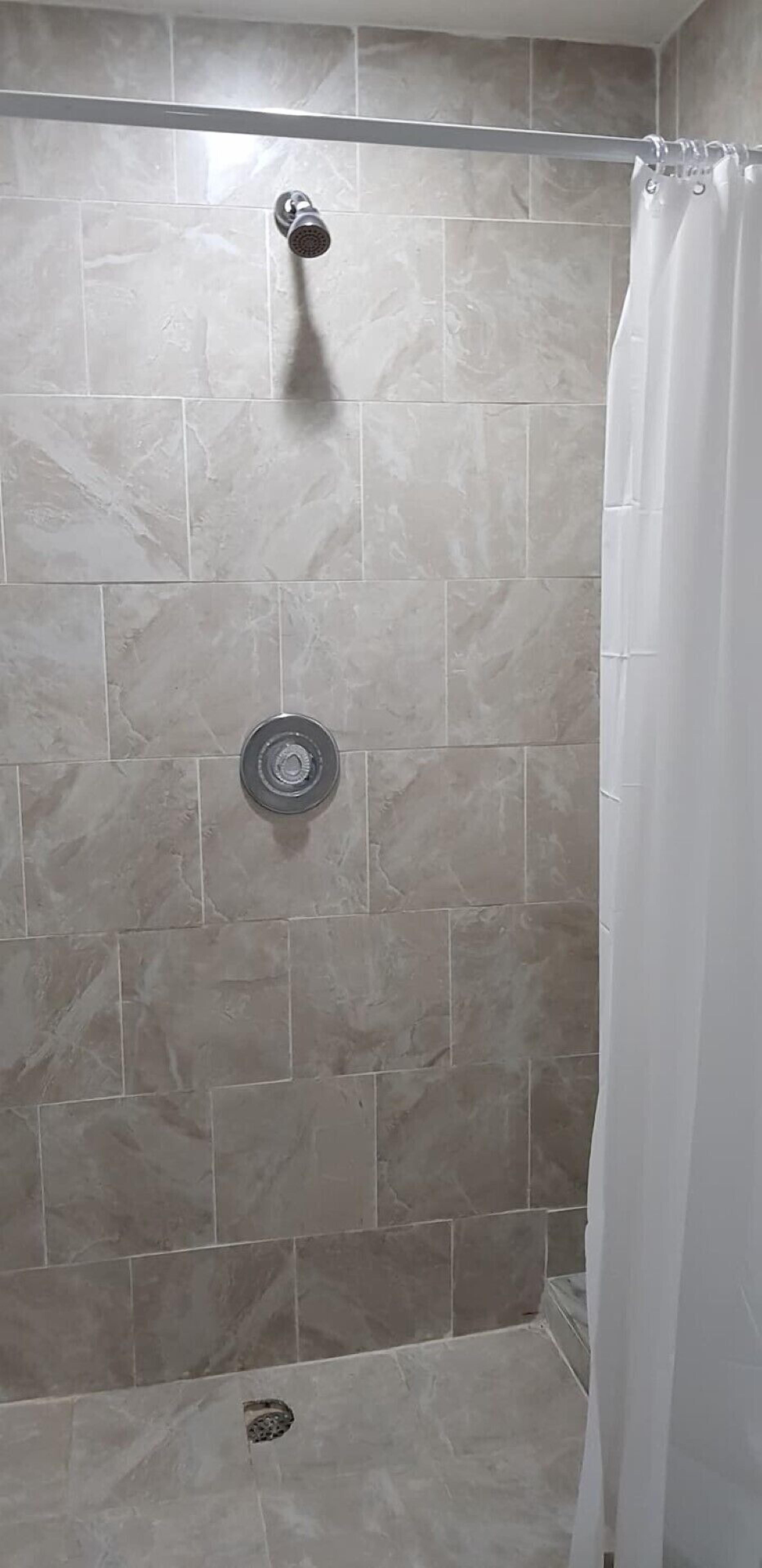 A shower area with beige tiles, a showerhead, and a curtain.