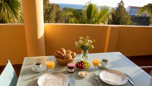 Et bord dækket til morgenmad med croissanter, frugt og drikkevarer på en balkon med udsigt over et smukt landskab.