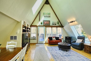 A cozy loft-style living space with a sloped ceiling, a dining area, a fireplace, and a large window offering a view of the outdoors. - Creekside Mountain Chalet with Hot Tub! Extended Stay (Black Hawk)