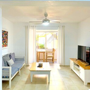 A living room with a sofa, a coffee table, a TV, and a balcony with a view.