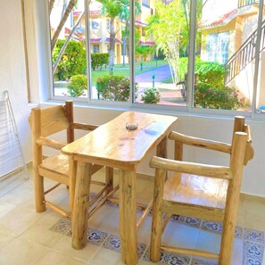 A wooden table and chairs in a room with a view of a courtyard through a large window. - Tropical A1 Apartment in Punta Cana on the Beach/Poolside (Punta Cana)