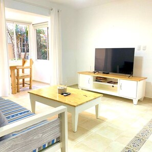 A living room with a television on a wooden stand, a coffee table with a glass and remote, and a striped sofa.