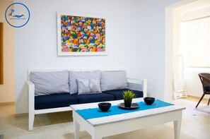 Un salon moderne avec un canapé blanc, une table basse surmontée d’un set de table bleu et un tableau abstrait aux couleurs vives accroché au mur.