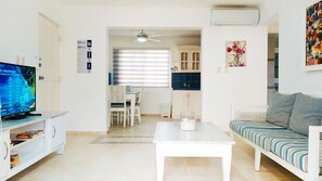 Un salon comprenant un téléviseur, un canapé blanc, une table basse et un coin repas avec une table et des chaises.