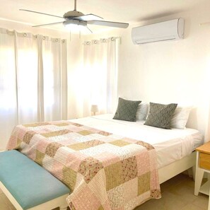 A bedroom with a bed, a bench, a ceiling fan, and an air conditioning unit.