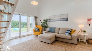 A modern living room with a sofa, ottoman, and a yellow armchair. There is a large window with a view of greenery outside. - Páteo Sagaipo - Villa Amália (Vale de Viga)