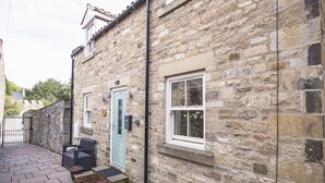 A stone building with a blue door, a window, and a small outdoor seating area with a table and chairs.