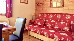 A cozy room with a wooden ceiling, a red sofa with a snow-themed print, a wooden table, and a chair. - AT THE FOOT OF THE CHAMPAGNY EN VANOISE SLOPES LA PLAGNE-PARADISKI PARC DE LA VANOISE (Champagny-en-Vanoise)