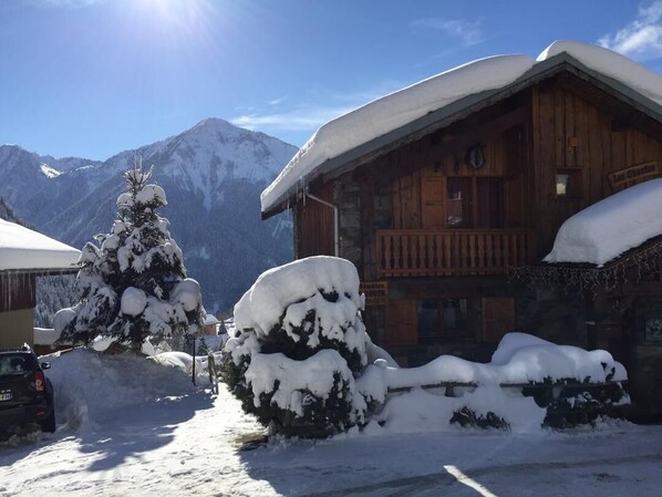 A wooden chalet with a balcony, surrounded by snow-covered trees and mountains in the background.