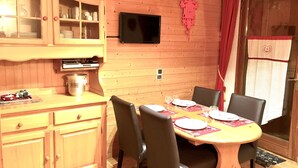 A wooden dining area with a table set for four, chairs, a television mounted on the wall, and a cabinet with glass doors. - AT THE FOOT OF THE CHAMPAGNY EN VANOISE SLOPES LA PLAGNE-PARADISKI PARC DE LA VANOISE (Champagny-en-Vanoise)