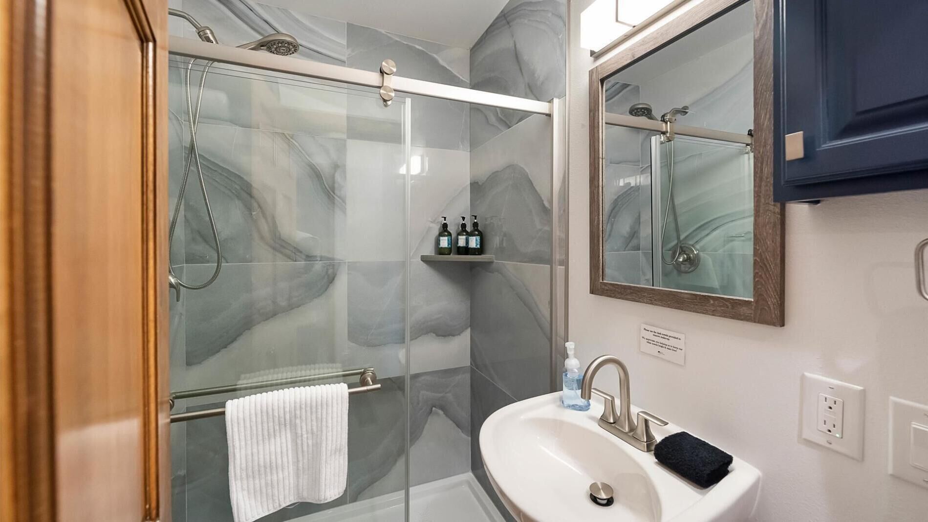 Een moderne badkamer met een douchecabine van glas, een wit wastafelmeubel en een spiegel erboven.