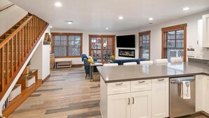 A spacious kitchen with a central island, wooden staircase, and a seating area with a sofa and chairs.