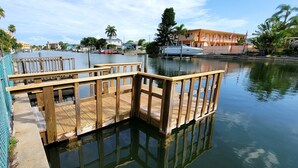 A wooden dock extending into calm water, surrounded by buildings and palm trees. - Satellite Motel - Happy Daze 107 (Treasure Island)