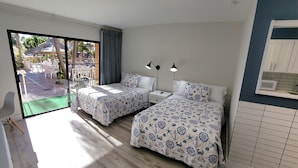 A bedroom with two beds, a large window, and a view of an outdoor patio area. - Satellite Motel - Happy Daze 107 (Treasure Island)