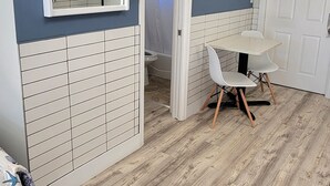 A room with a wooden floor, a white table with two chairs, a white door, and a mirror on the wall. - Satellite Motel - Happy Daze 107 (Treasure Island)