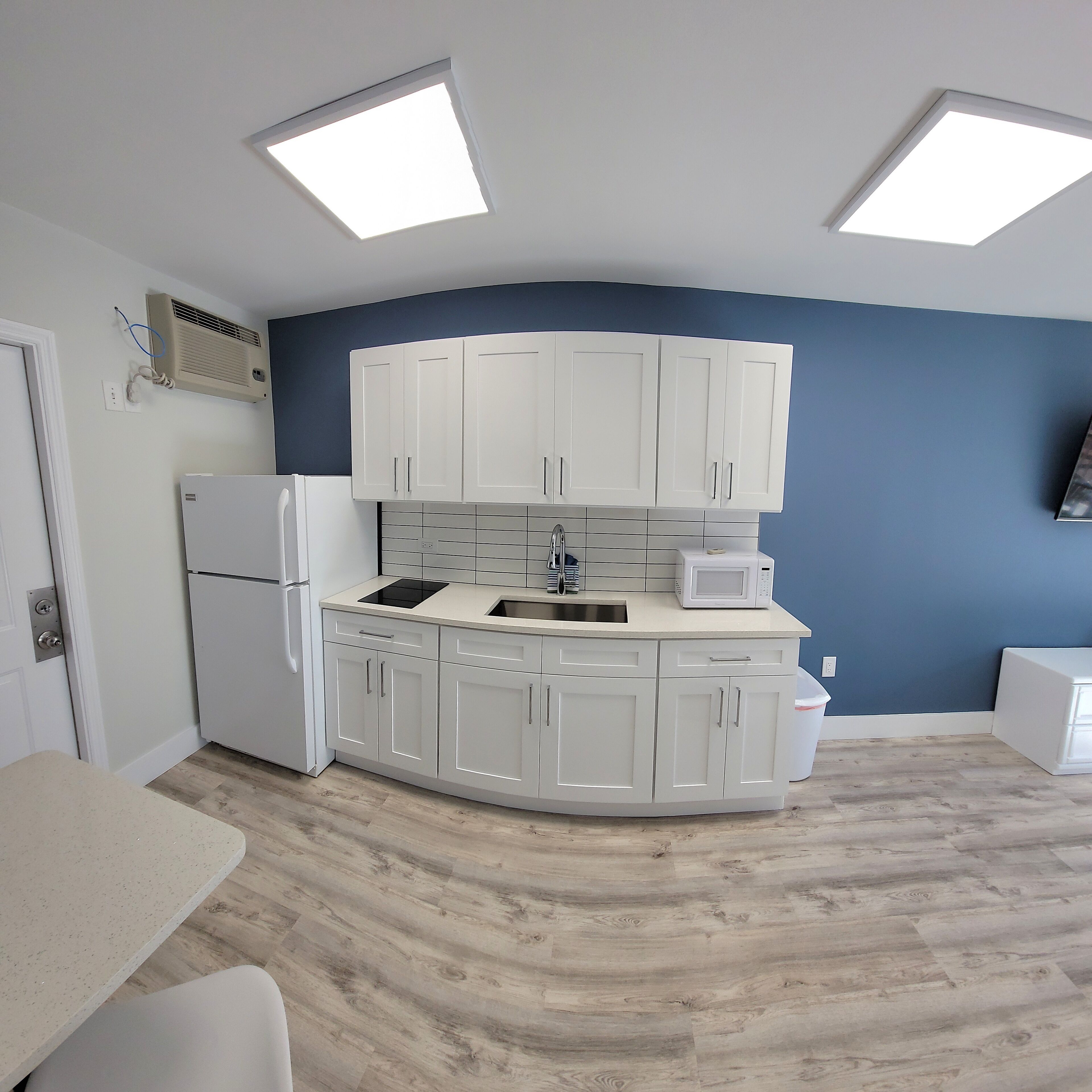 A modern kitchen with white cabinets, a built-in microwave, and a refrigerator.